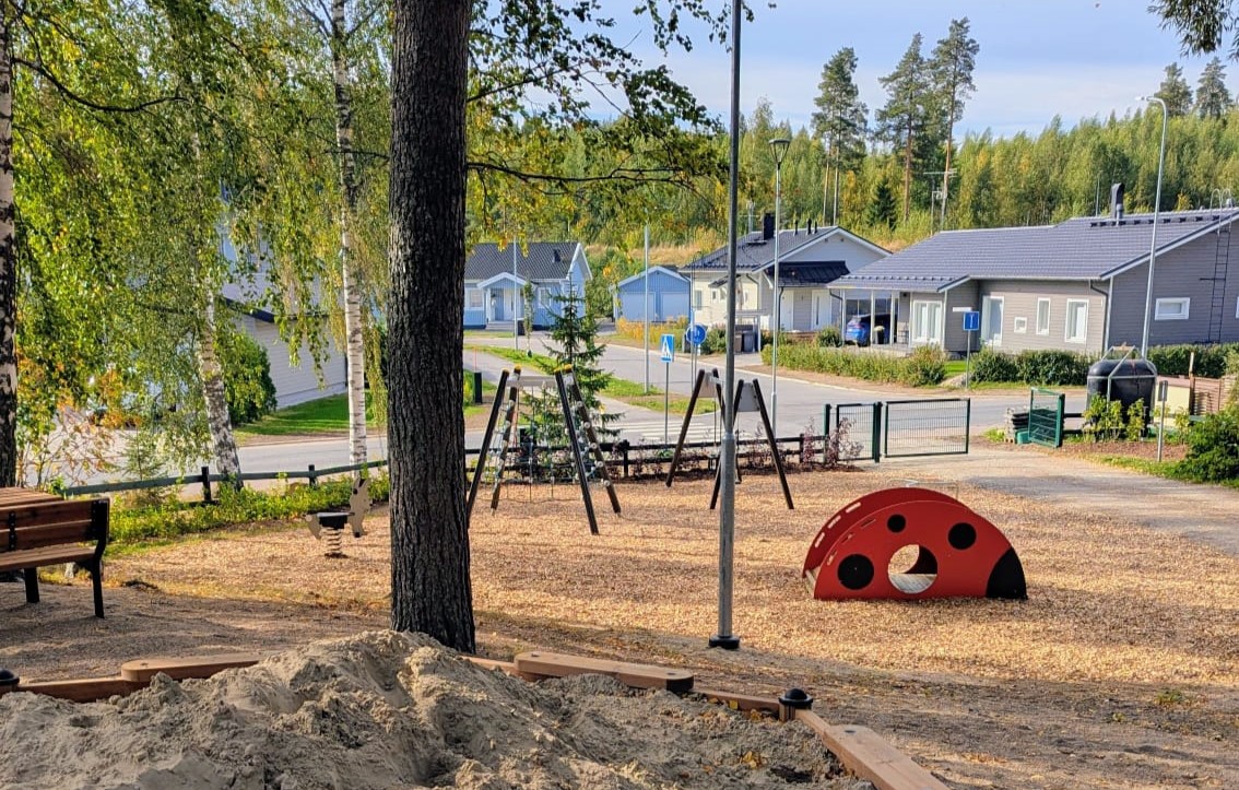 Leikkipuistoa, hiekkalaatikko ja telineitä, takana omakotitaloasutusta.